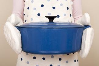 blue cooking pot being held by a cook with oven mitts.